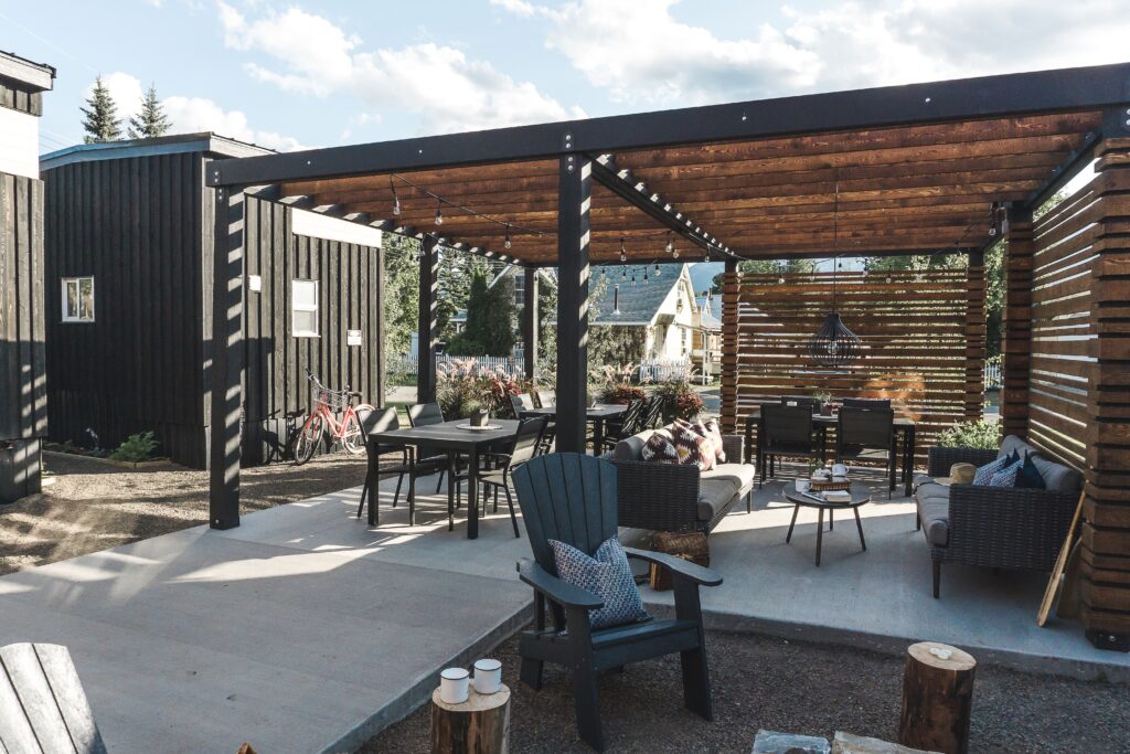 It is the outside area of a coffee shop. There are tables with decorations in the middle. Each table has its chairs and booths. A few chairs have pillows.